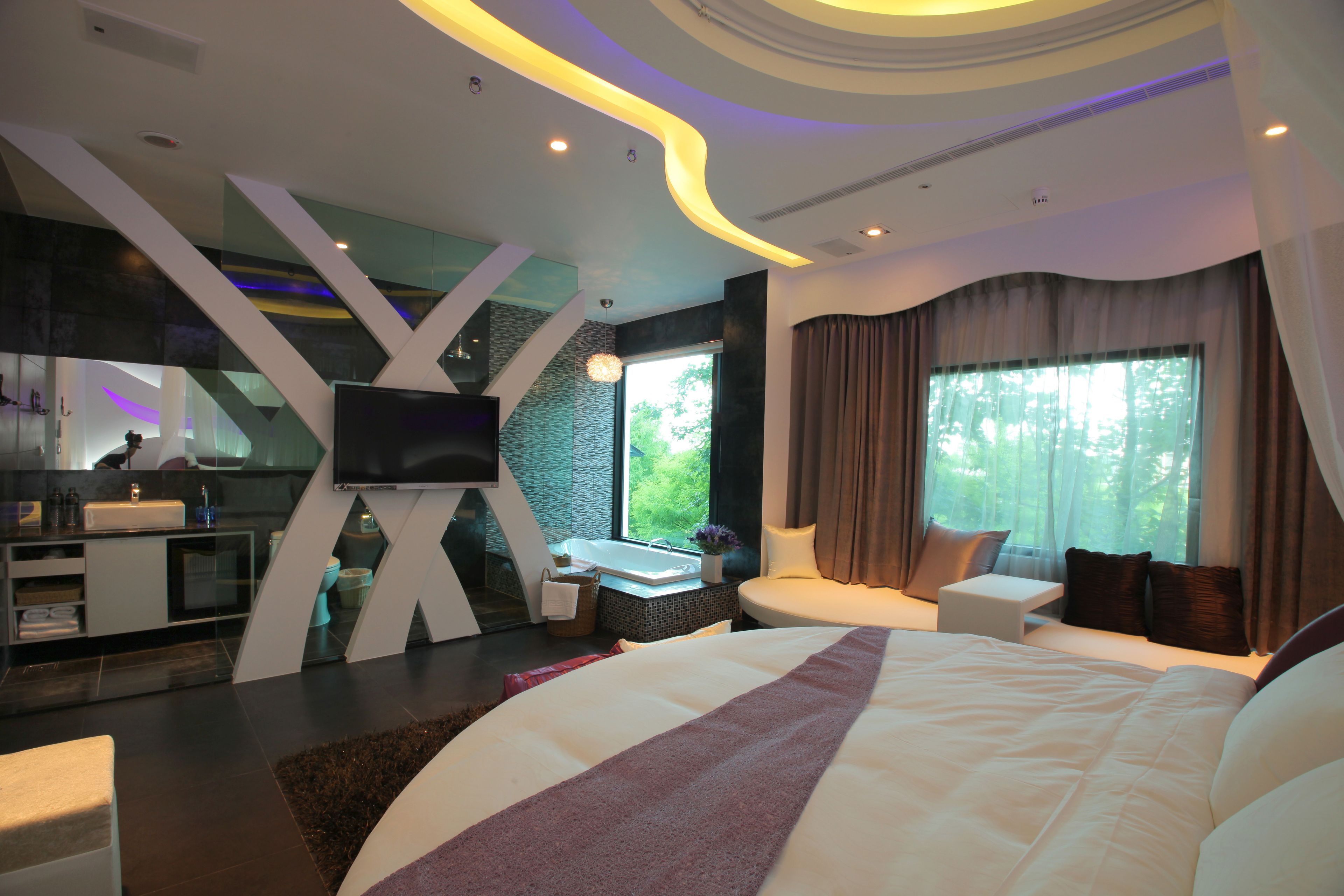 A modern hotel room with a large bed, a sitting area, a TV, and a bathroom with a bathtub.