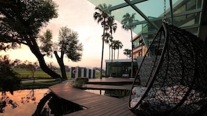 A modern outdoor area with a wooden deck, a hanging chair, and a view of a building with glass windows. - Maple House Riverside (Dongshan)