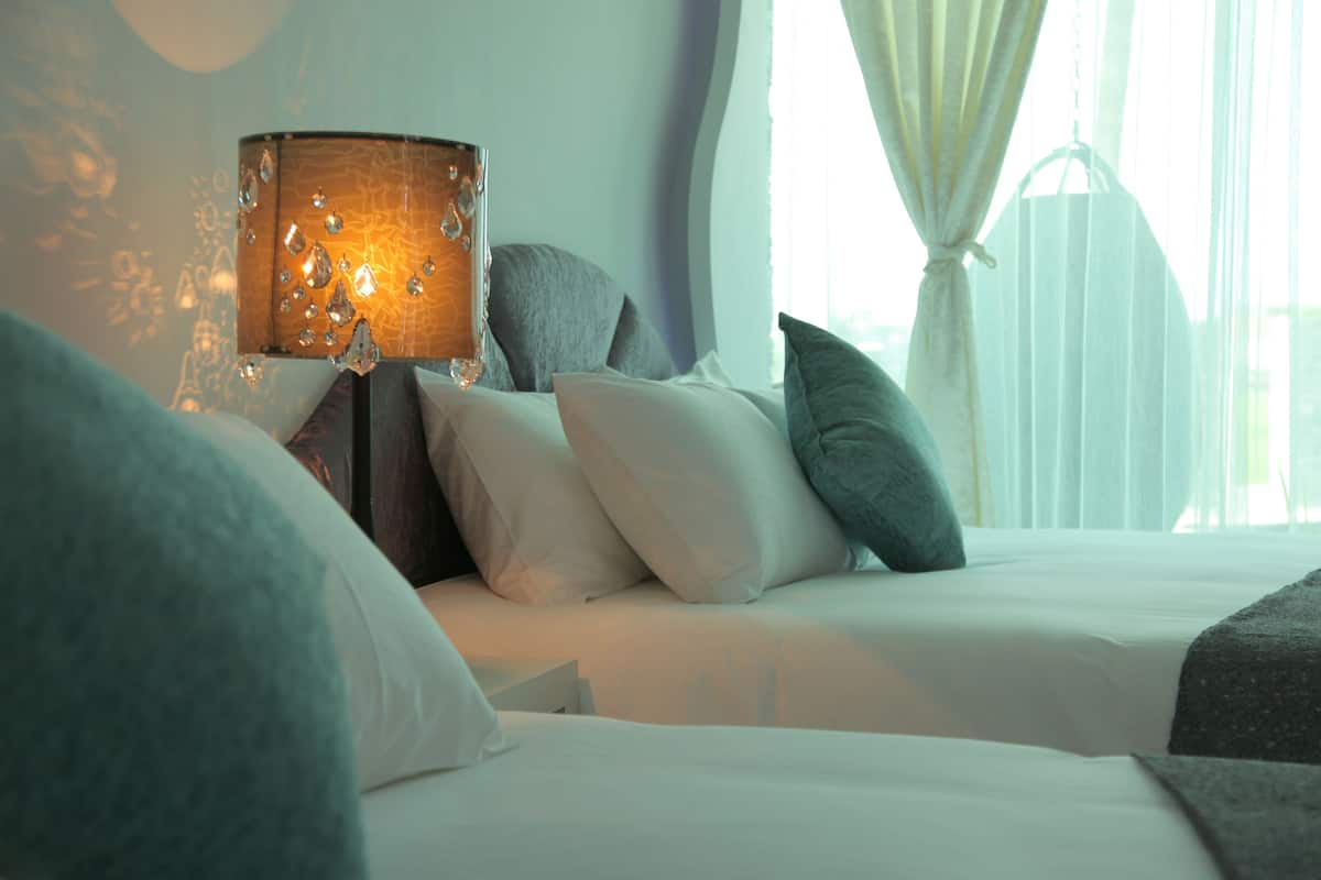Cama bem arrumada com roupa de cama branca e abajur com cúpula texturizada.