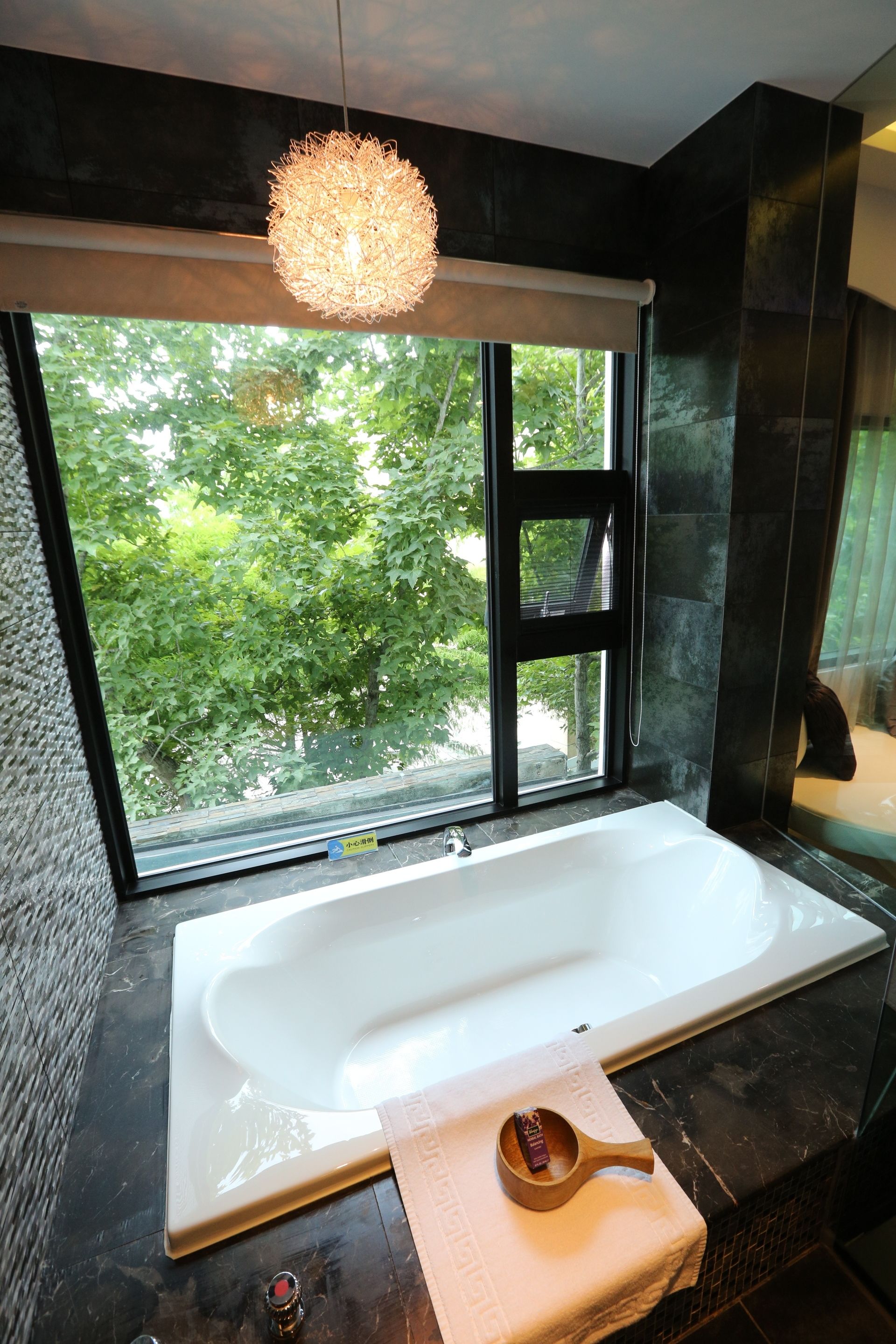 Ein modernes Badezimmer mit einer großen Badewanne, einem Fenster mit Blick auf Grünflächen und einer hängenden Leuchte.