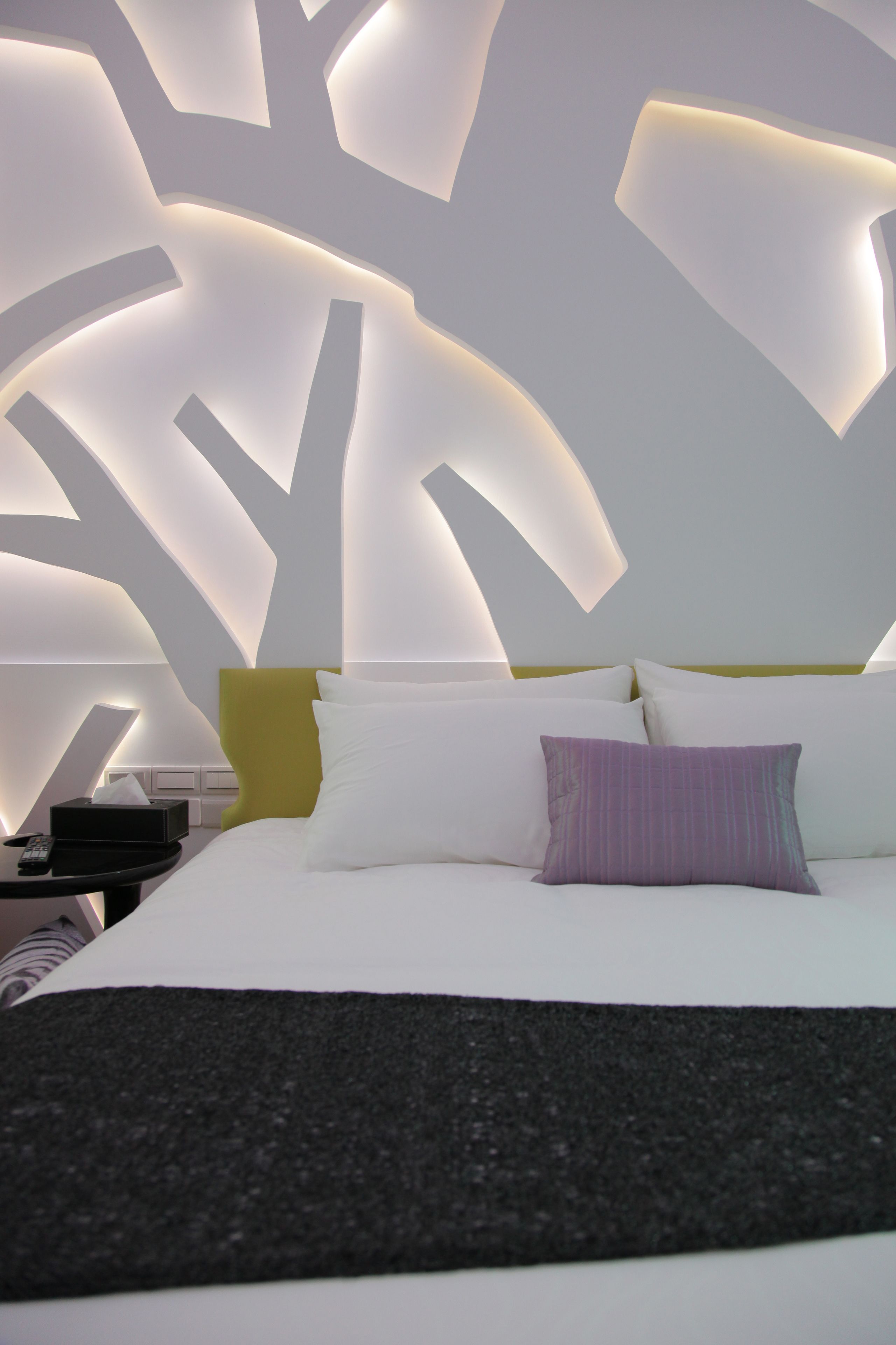 Una habitación de hotel moderna con una cama grande, una mesita de noche y un diseño de pared original.