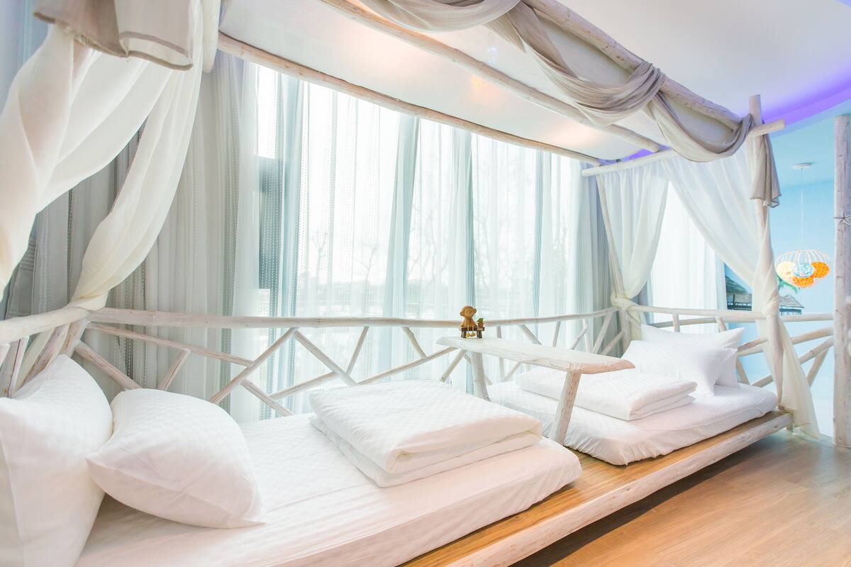 Quarto com cama, uma pequena mesa e janela com cortinas leves.