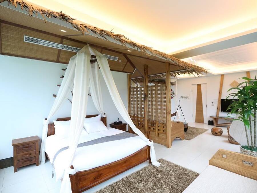 A modern bedroom with a canopy bed, a wooden headboard, a small bedside table, and a large potted plant.