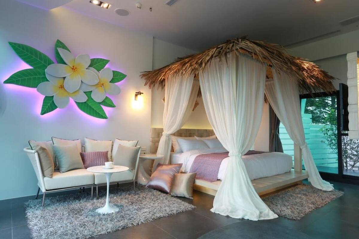 Quarto moderno com cama de dossel, sofá e decoração floral na parede.