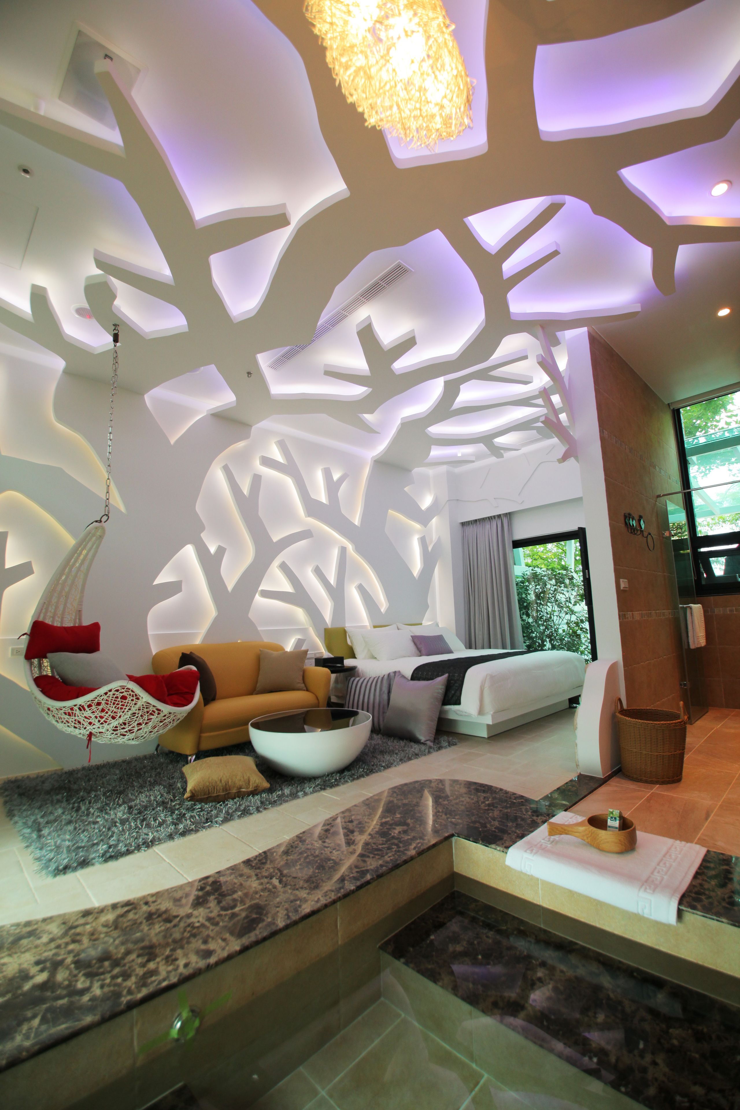 A modern interior with a unique ceiling design, a hanging chair, a sofa, and a small seating area with a table.