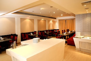 Un espace de restauration moderne dans un hôtel, avec de nombreuses tables et chaises, un comptoir central blanc et un mur à la texture de pierre.