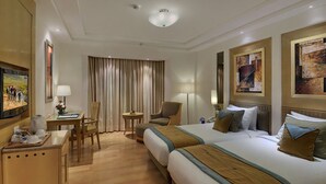 A hotel room with two beds, a desk, a chair, a small table, and a TV.