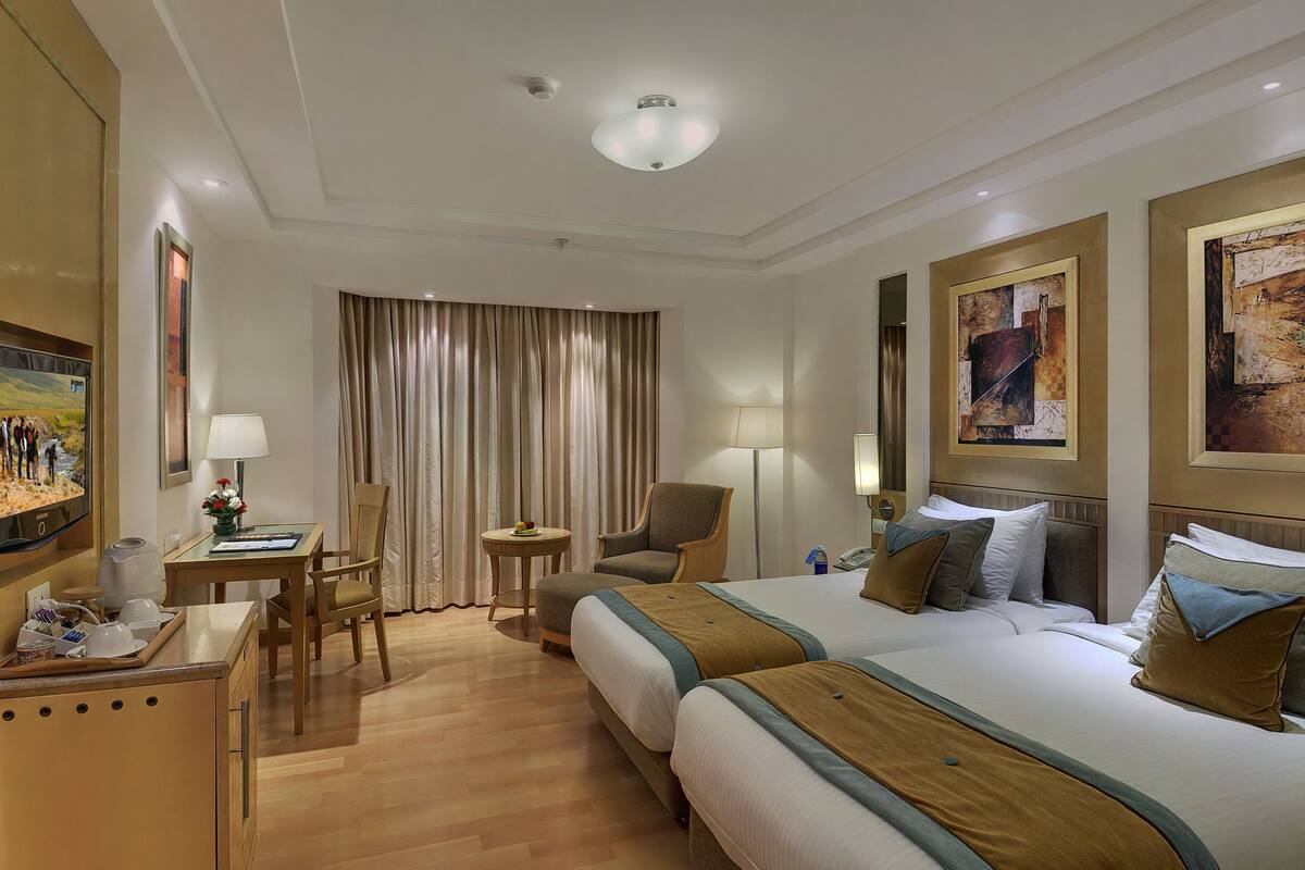 Habitación de hotel con dos camas, un escritorio, una silla, una mesita y un televisor.