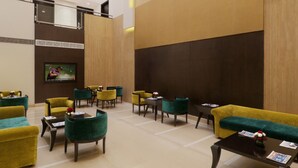 A spacious lobby with multiple seating areas, a television screen, and a large painting on the wall.