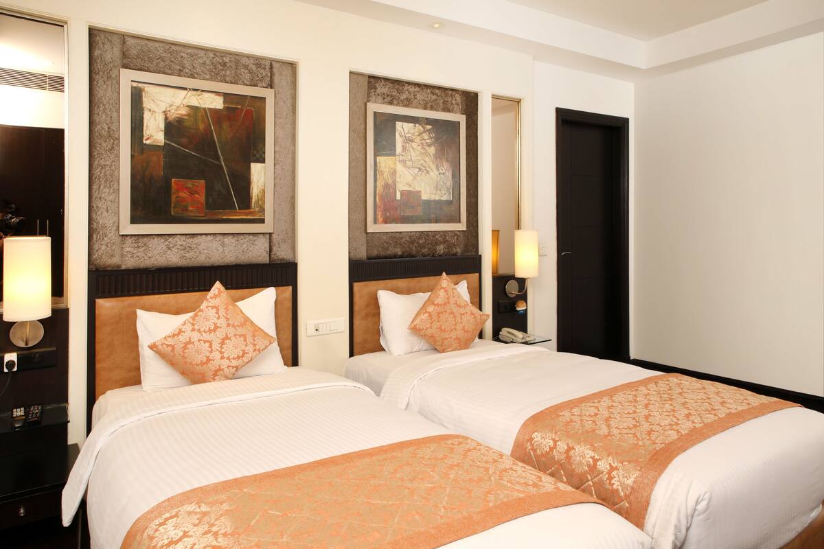 Habitación de hotel con dos camas, cada una con una colcha estampada, cabeceros con diseño texturizado y un cuadro abstracto enmarcado sobre las camas.