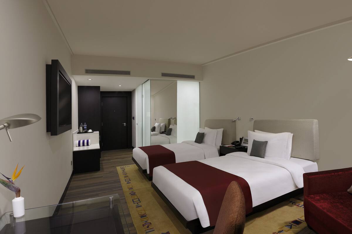 A hotel room with two beds, a red sofa, a desk, a TV, and a mirror.