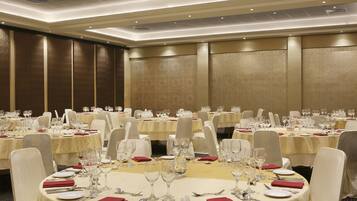 A banquet hall with round tables set for dining, equipped with cutlery, glasses, and red napkins.
