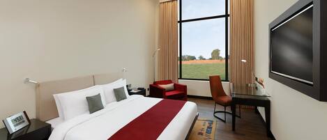 Habitación de hotel con cama, escritorio, silla, televisor y ventana con vistas a un campo.