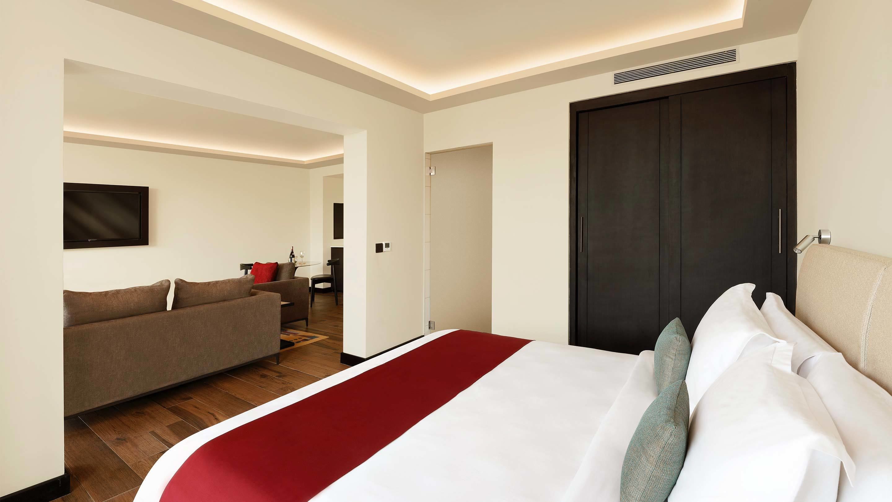 Une chambre d’hôtel avec un grand lit, un canapé, un téléviseur fixé au mur et une porte sombre.