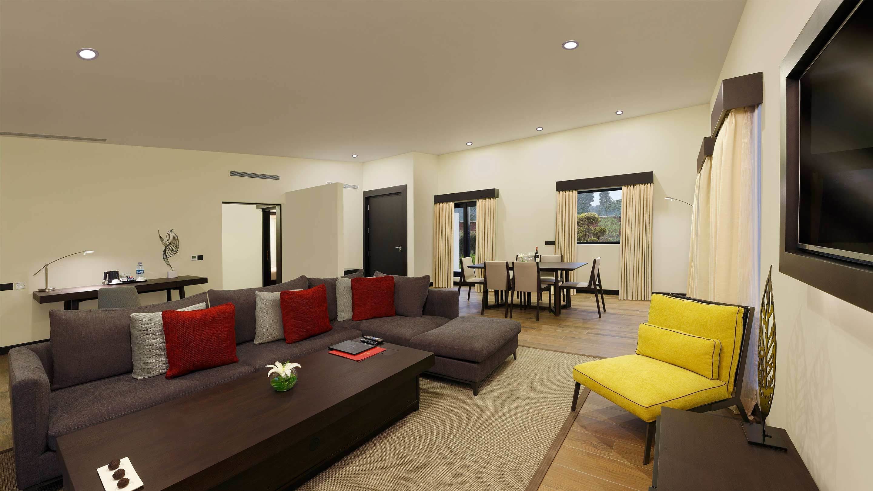 Una sala de estar moderna con un sofá seccional, un sillón amarillo, una mesa de centro y un comedor con mesa y sillas.