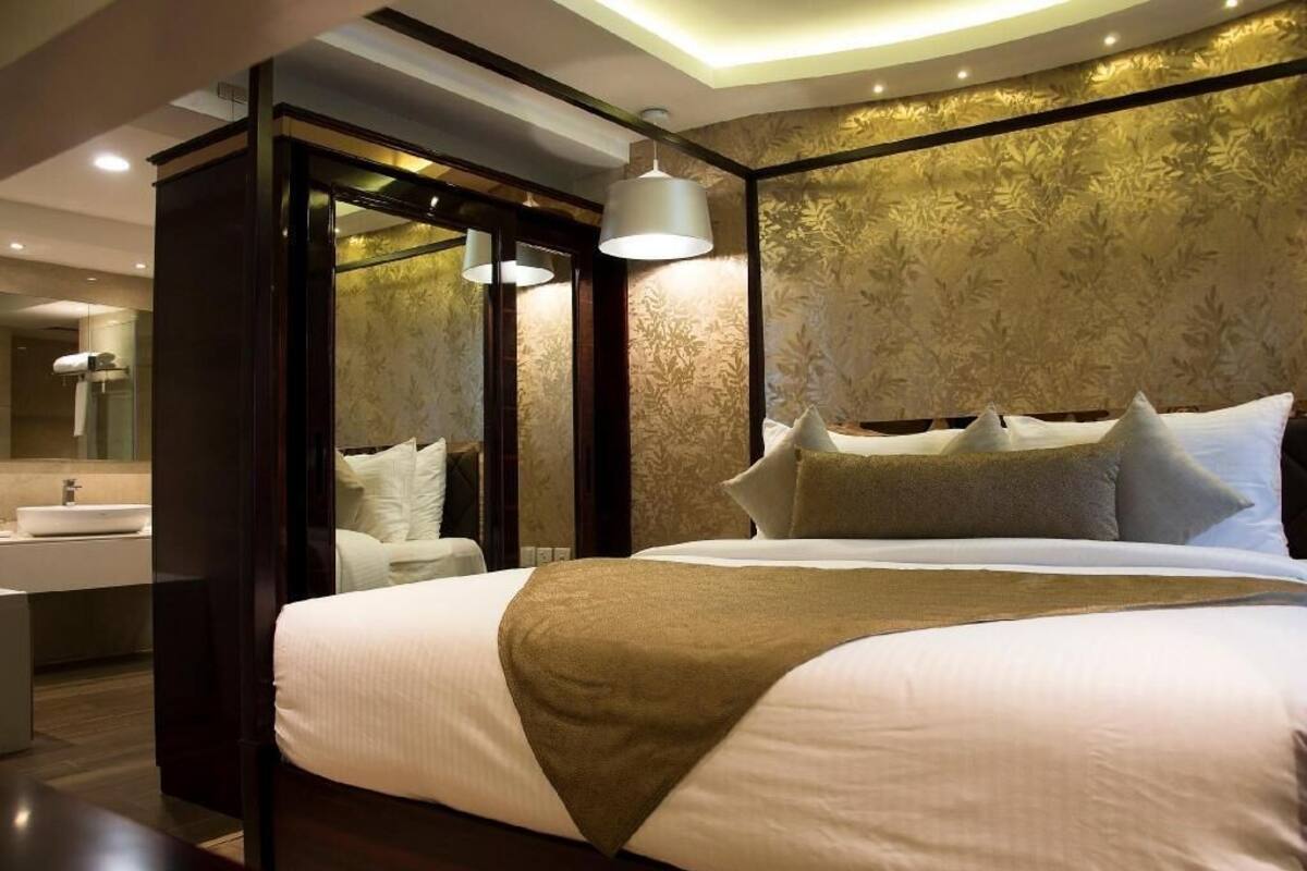 A hotel room with a large bed, a bedside table, a mirror, and a bathroom with a sink and shower.