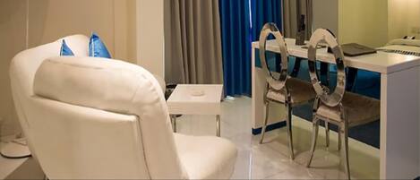 Una sala de estar moderna con un sofá blanco, una mesa de comedor con sillas, un televisor de pantalla plana montado en la pared y un amplio ventanal con cortinas azules.