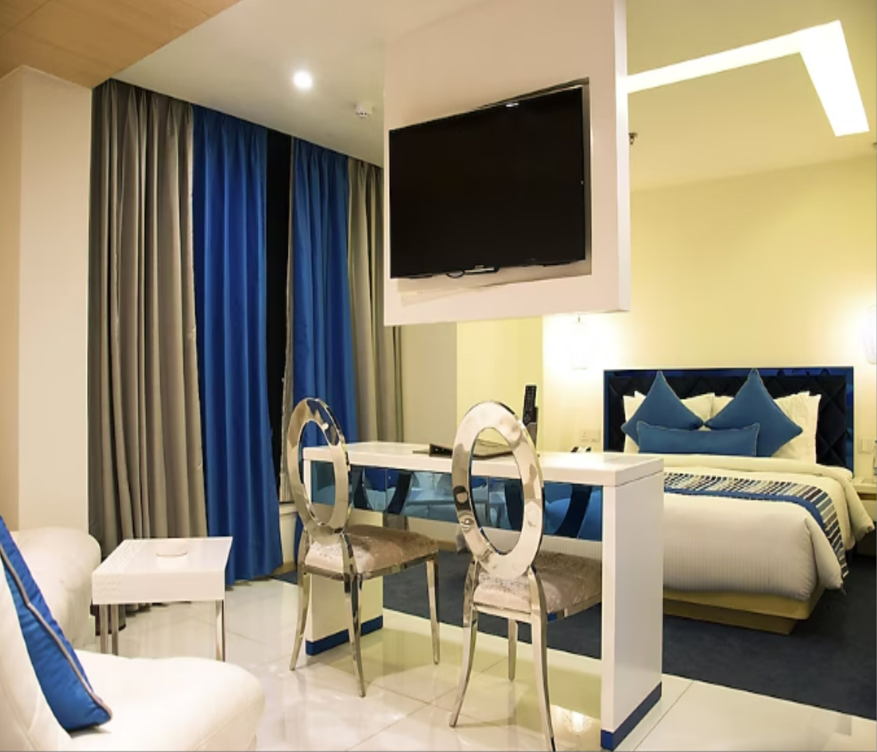 Ein Hotelzimmer mit einem Bett, einem Schreibtisch mit Stuhl, einem an der Wand befestigten Fernseher und einem Fenster mit Vorhängen.