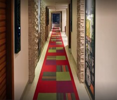 A hallway with a colorful carpet, stone pillars, and a framed picture on the wall.