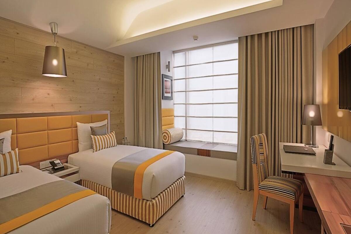 A hotel room with a large bed, a desk, a chair, a window with curtains, and a ceiling light.