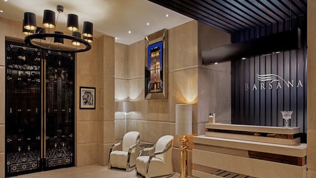 A reception area with a modern design, featuring a reception desk, two armchairs, a patterned carpet, and a chandelier.