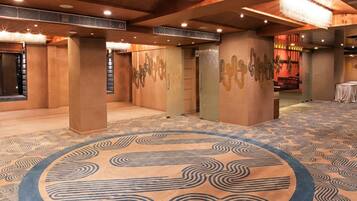 A spacious hall with patterned carpet, wooden pillars, and a chandelier.