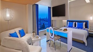 A modern hotel room with a bed, a desk, a chair, and a TV.