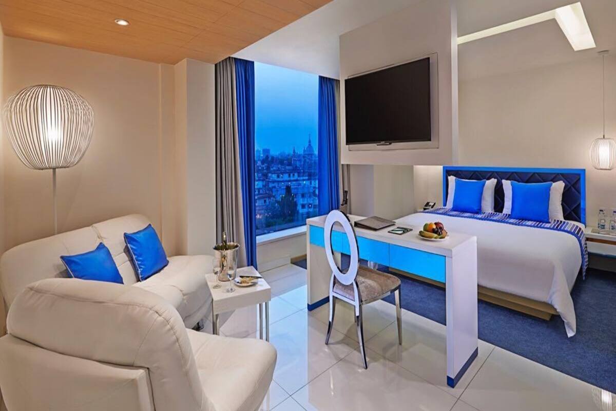 A modern hotel room with a bed, a desk, a chair, and a TV.