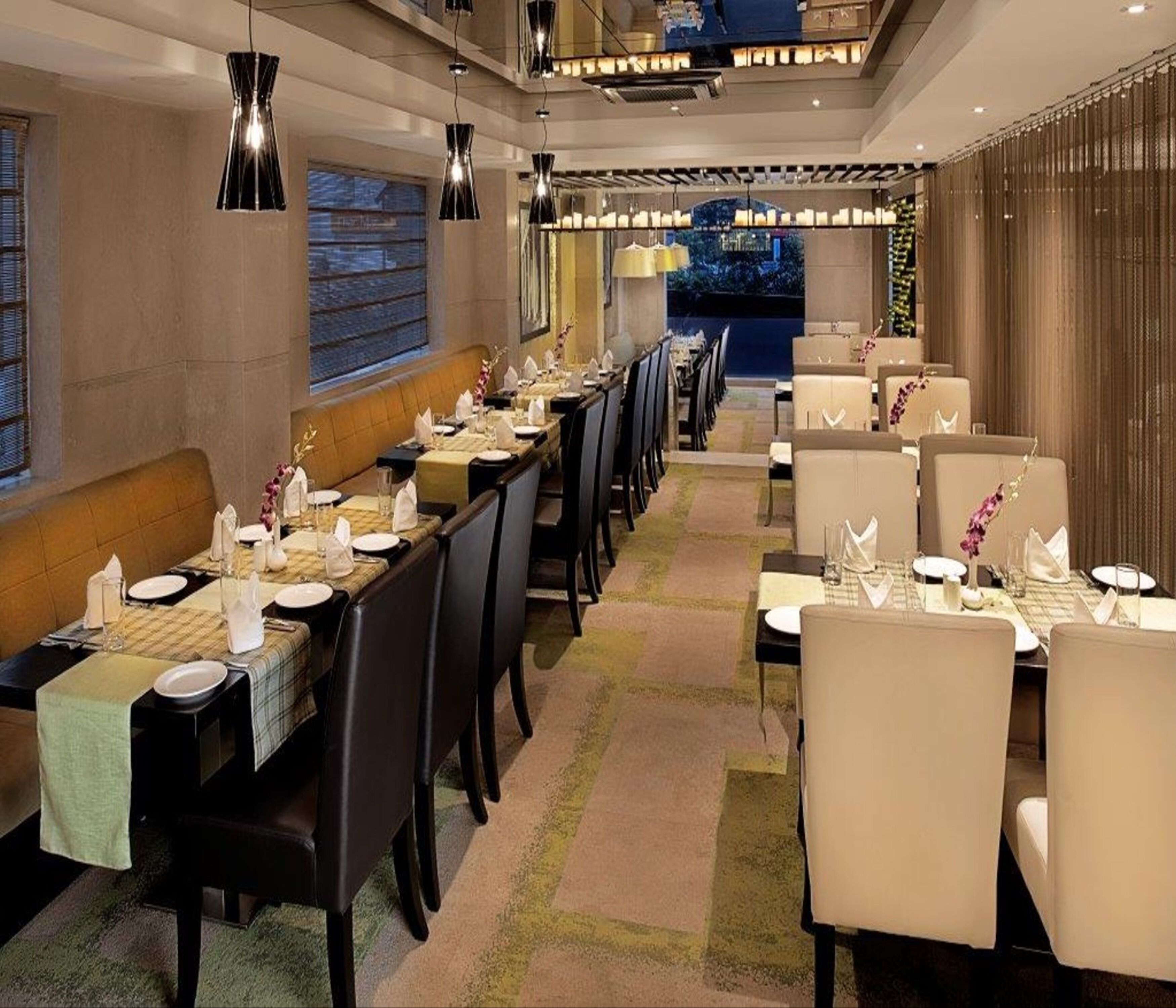 A restaurant with long tables, chairs, and hanging pendant lights.