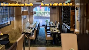 A restaurant with a long table set for dining, a view of greenery outside, and a modern ceiling design.