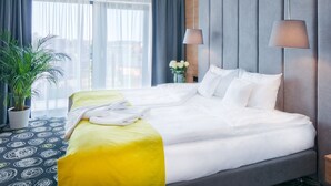 Habitación de hotel con una cama grande, una planta en maceta, un florero con flores y vistas a la ciudad.