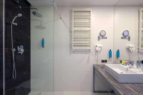 Un baño moderno con ducha envuelta en vidrio, un lavamanos blanco sobre encimera de mármol y dos espejos fijados a la pared.
