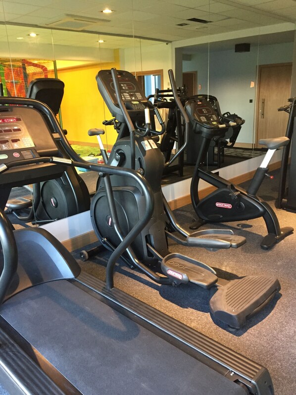 A row of stationary bikes in a gym with a mirrored wall and a yellow wall in the background. - Baltin Hotel & SPA (Mielno)