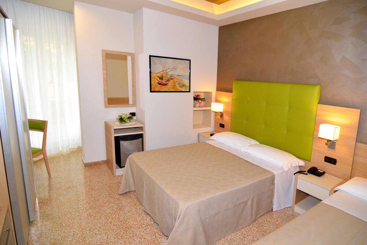Una habitación de hotel con una cama grande, una mesita de noche con lámpara, un escritorio pequeño, una silla y un cuadro en la pared.