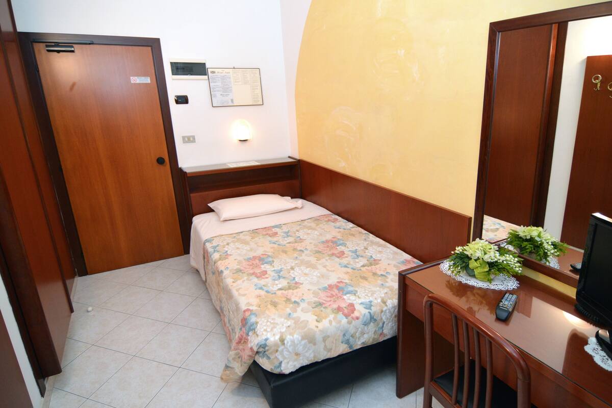 Una habitación pequeña con cama, escritorio, silla, espejo y televisor.
