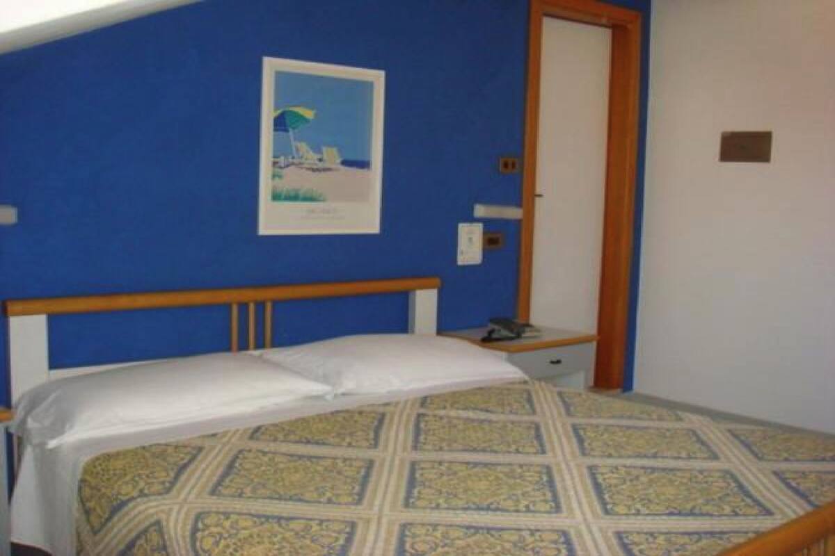 Un dormitorio con cama, mesita de noche, un cuadro enmarcado en la pared y una puerta.