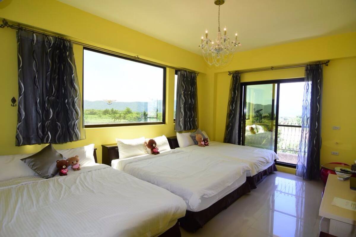A hotel room with two beds, a chandelier, and large windows with curtains.