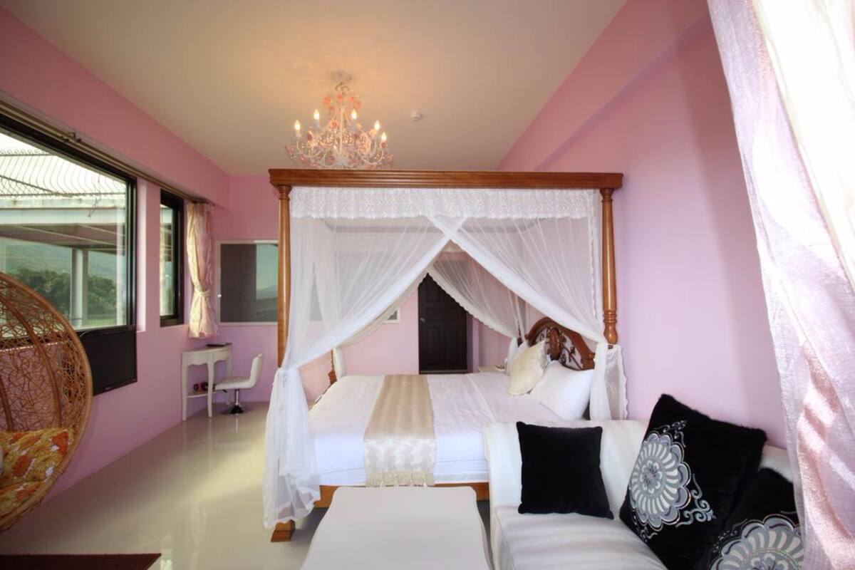 A four-poster bed with a canopy, a chandelier, and a view of the outdoors through a large window.