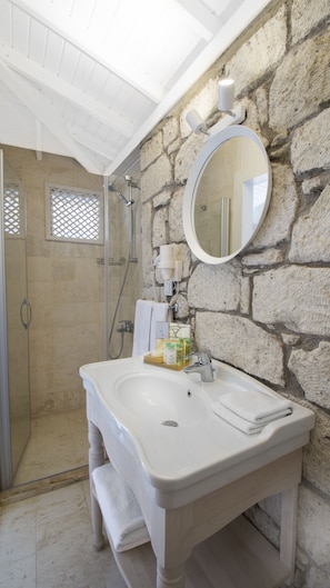 A bathroom with a stone wall, a white sink, a mirror, and a shower area.
