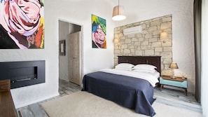 Ein Schlafzimmer mit Steinwand, einem Bett mit weißen Bettwäsche, einem Holz-Kopfteil, einem Nachttisch mit Lampe und Bildern an den Wänden.