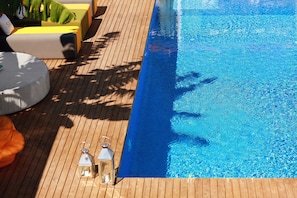 Eine Holzterrasse mit Pool, gelb-grauen Liegestühlen und zwei transparenten Laternen.