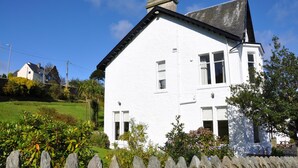 A white two-story house with a gabled roof, surrounded by a stone fence and lush greenery. - Kames Hotel (Tighnabruaich)