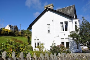 A white two-story house with a gabled roof, surrounded by a stone fence and lush greenery. - Kames Hotel (Tighnabruaich)