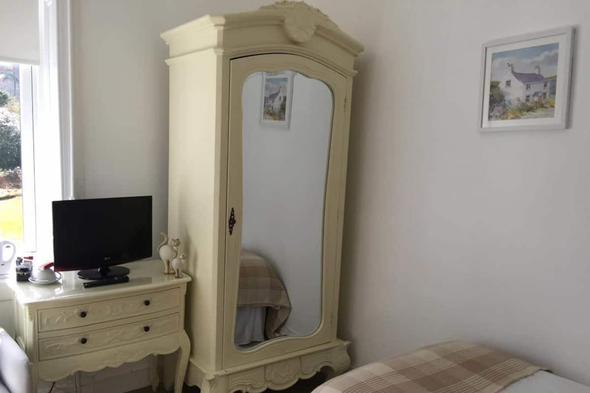 A bedroom with a white wardrobe, a television on a side table, and a bed with a plaid blanket.