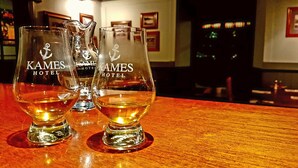 Drie glaasjes drank op een houten bar met de tekst 'KAMES HOTEL' erop.