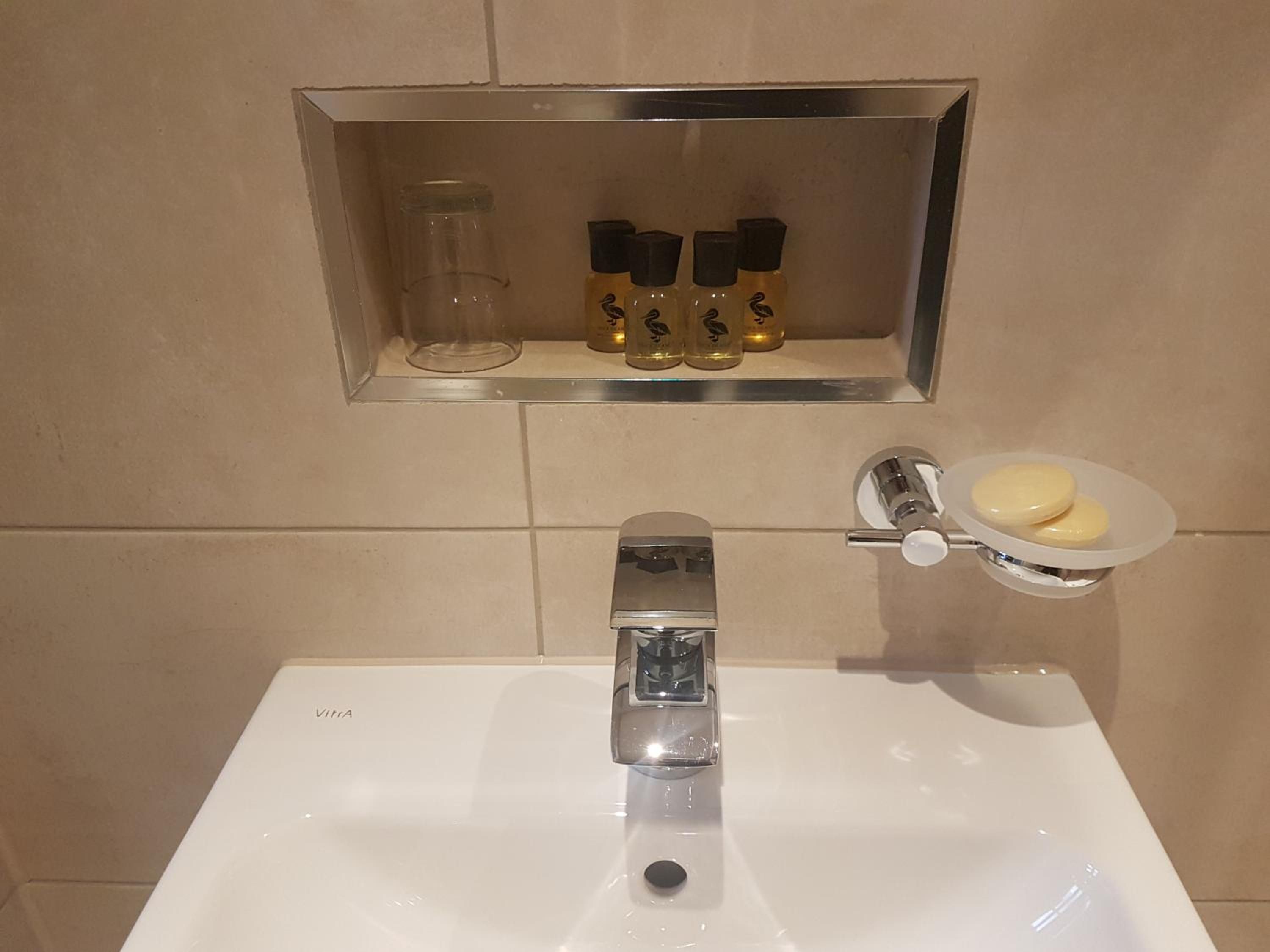 Un baño con un lavabo blanco, un tarro de cristal y tres botellas con tapones negros.