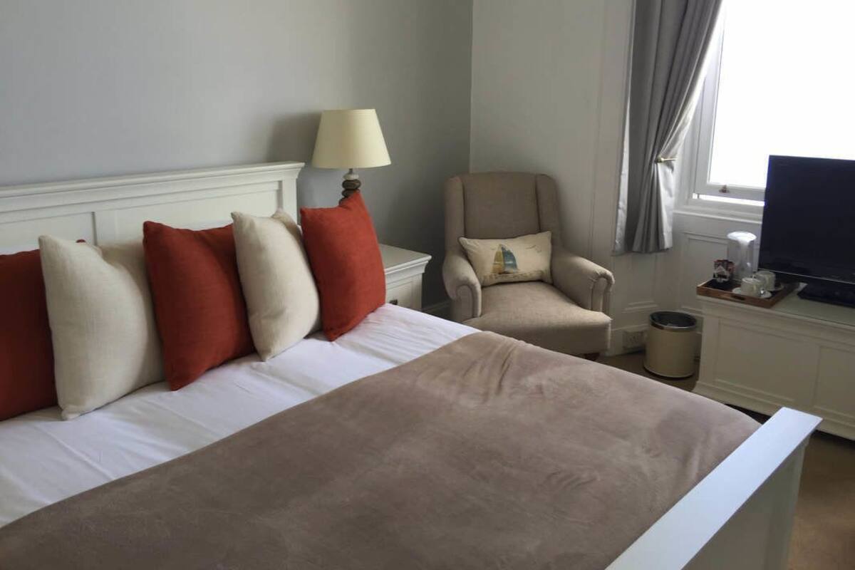 A hotel room with a bed, a chair, a lamp, a television, and a window with curtains.