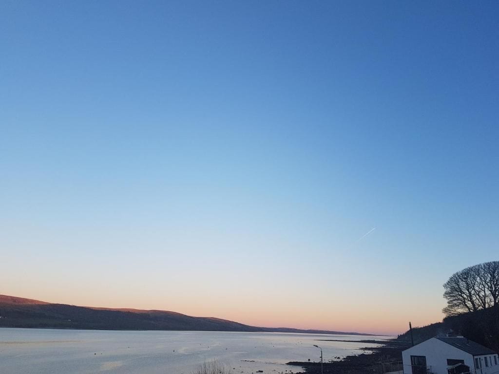 A coastal landscape with a clear sky, a body of water, and a small white building.