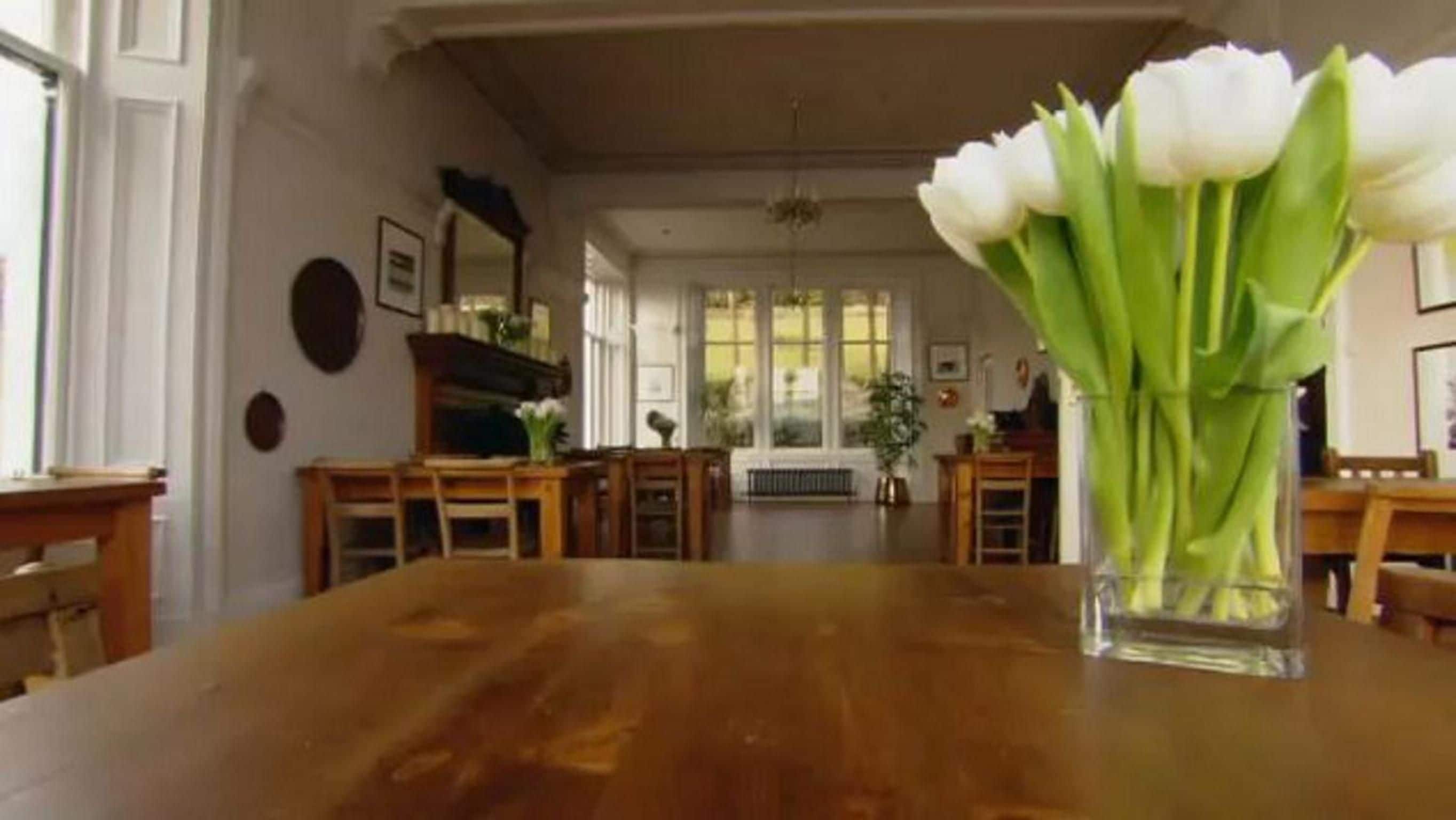 Een eetkamer met een houten tafel, stoelen en een vaas witte bloemen.