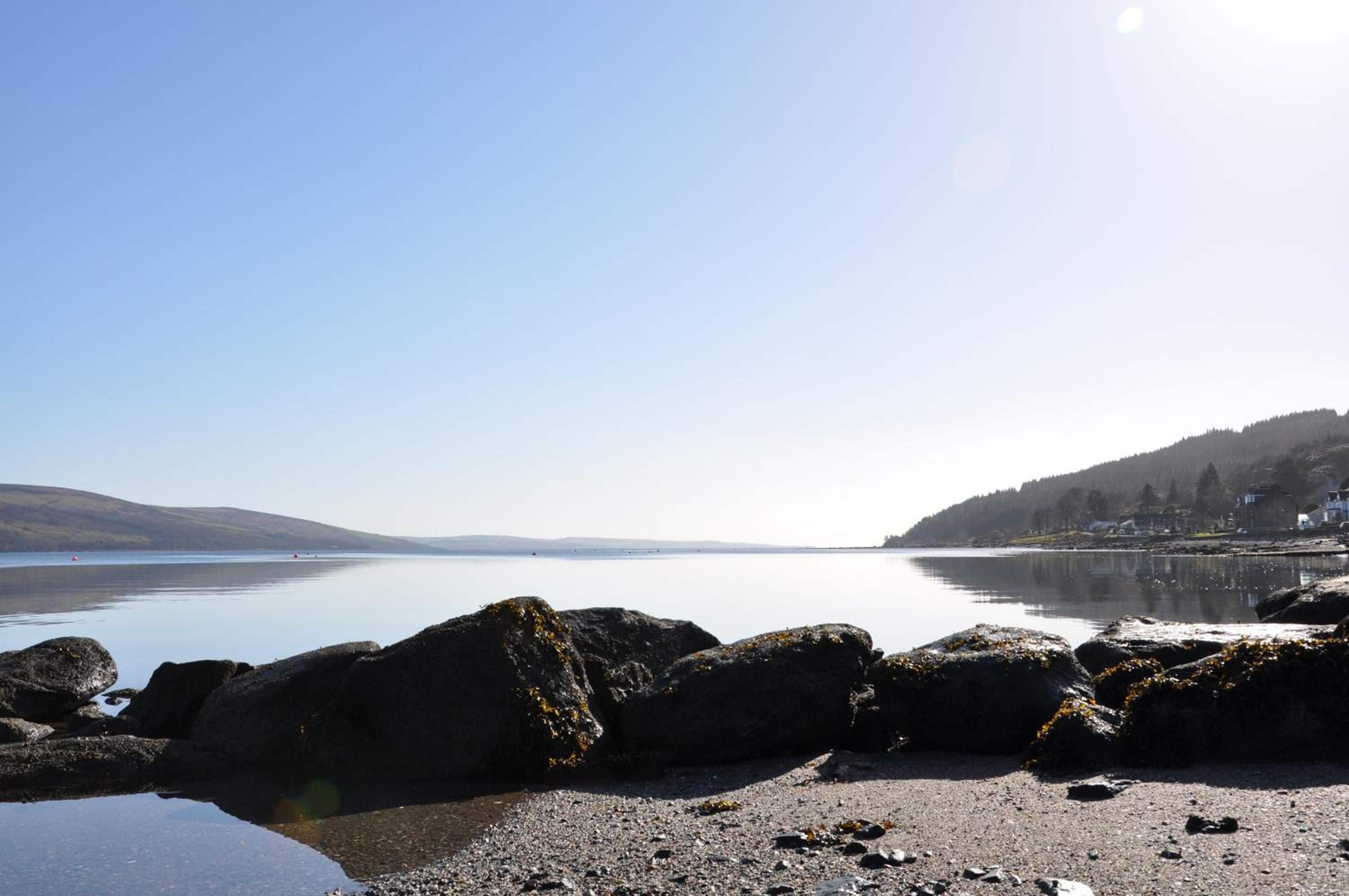 A calm lake with rocky shores and a distant shoreline with buildings.